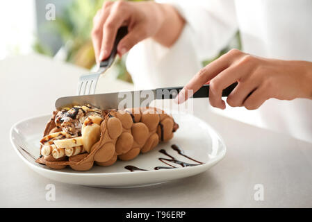 Woman eating sweet bubble waffle à table Banque D'Images