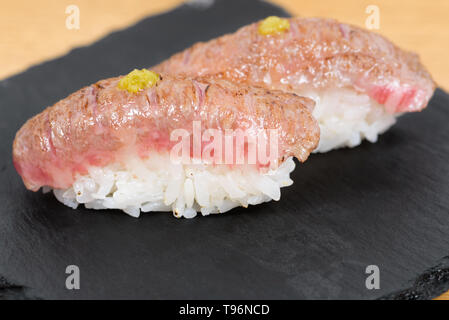 Nigiri de chaleur-gravé kobé habillés avec de la moutarde, servis sur une plaque carrée de l'ardoise, l'arrière-plan de table en bois Banque D'Images