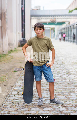 Cheerful Young boy standing on street tout en tenant une planche à roulettes tandis que à la caméra dans un jour lumineux Banque D'Images