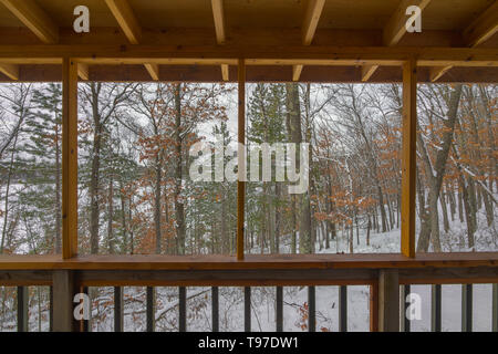 Belle vue d'un hiver enneigé Northwoods forêt mixte (feuillus et conifères) par un porche sur un chalet rustique sur un lac éloigné dans Banque D'Images