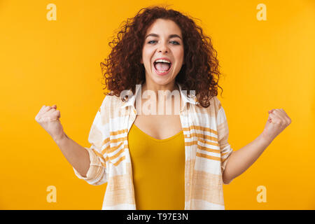 Image de femme extatique 20s avec les cheveux bouclés de crier et de réjouissance, isolé sur fond jaune Banque D'Images