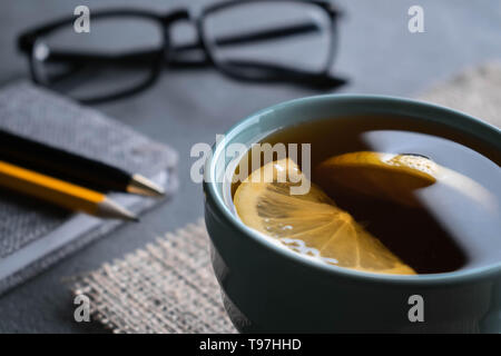 Thé noir avec deux morceaux de citron sur une serviette de toile avec un petit gris le bloc-notes, stylo noir un crayon et verres Banque D'Images