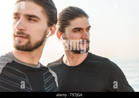 Close up of a deux frères jumeaux faisant des exercices à la plage ensemble, wearing earphones Banque D'Images