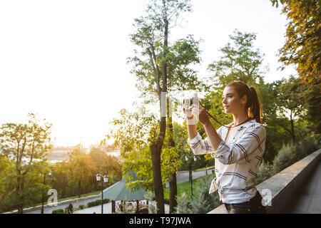 Souriante jeune fille pour prendre des photos avec l'appareil photo tout en se tenant au parc Banque D'Images