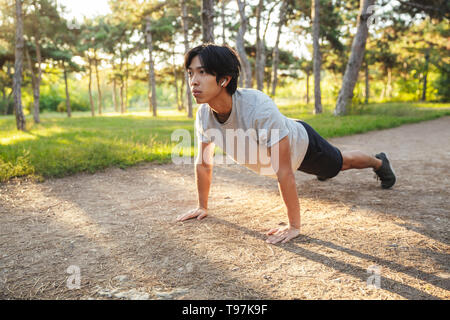 Certains jeunes athlètes asiatiques homme portant des vêtements de sport de faire les exercices à l'extérieur dans le parc, faisant de l'exercice de planches Banque D'Images