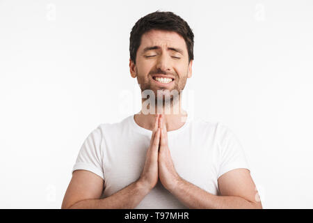 Image homme 30s avec en soie t-shirt holding paumes ensemble et priant isolé sur fond blanc Banque D'Images