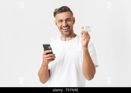 Image de bel homme 30s portant des T-shirt holding smartphone et carte de crédit en plastique isolé sur fond blanc Banque D'Images