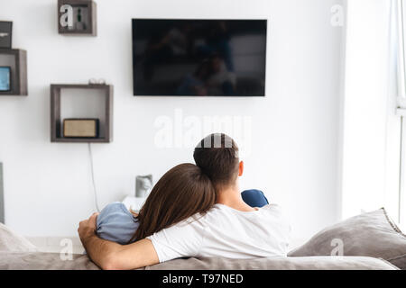 Droit de l'arrière de l'heureux couple homme et femme dans les vêtements de regarder la télévision sur un canapé à la maison Banque D'Images