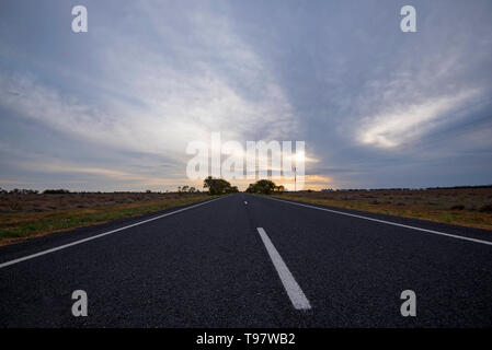 Des nuages de pluie et le coucher du soleil sur une longue ligne droite de l'autoroute Kamilaroi près de Burren Junction dans l'ouest de la Nouvelle-Galles du Sud, Australie Banque D'Images