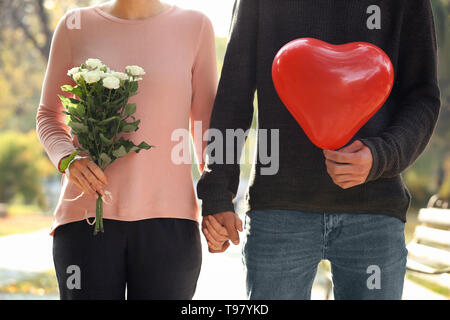 Jeune couple aimant avec ballon en forme de coeur et fleurs à l'extérieur date romantique Banque D'Images