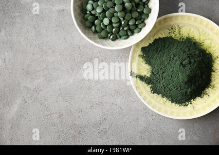 Les plaques avec la spiruline en comprimés et poudre sur table gris Banque D'Images