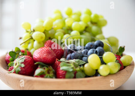 Bol en bois avec fruits : fraises, bleuets et raisins verts. Banque D'Images