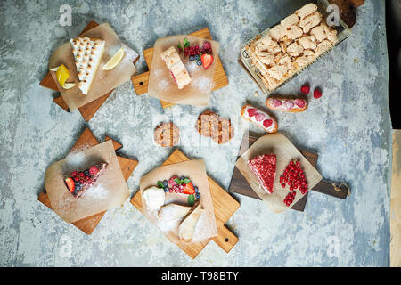 Assortiment de desserts sucrés : gâteaux, churos, rouleau de meringue, crème glacée, décorées avec des baies sur les planches de bois. Vue d'en haut. Fond texturé gris. Beaux plats de service. Le Dessert. La chaîne alimentaire Banque D'Images