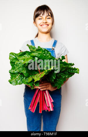 Happy girl en salopette denim holding a bunch of fresh de blettes. Se concentrer sur les feuilles Banque D'Images