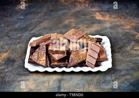 Morceaux de chocolat heap avec la poudre de cannelle sur la plaque en céramique blanche. Sweet Food concept photo. Les morceaux de chocolat noir cassé empilées sur backg Banque D'Images