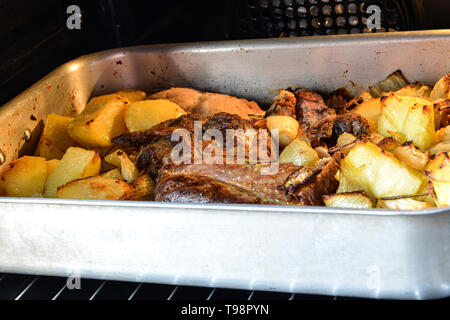 Rôti avec des pommes de terre dans un plat de cuisson en aluminium dans le four. Banque D'Images