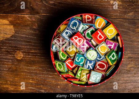 Tin Can plein de carreaux de céramique colorés avec des lettres sur la texture du bois Banque D'Images