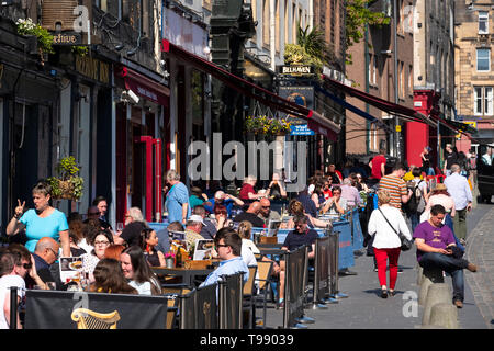 Beaucoup de gens boire ou manger à l'extérieur dans le soleil chaud dans les bars et cafés sur Grassmarket dans la vieille ville d'Édimbourg, Écosse, Royaume-Uni Banque D'Images