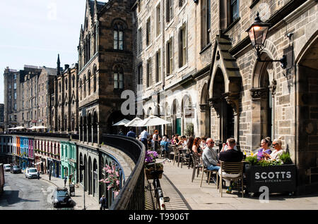 Les gens de boire et manger dans les restaurants de beau temps sur la terrasse au-dessus de Victoria Victoria Street dans la vieille ville d'Édimbourg, Écosse, Royaume-Uni Banque D'Images