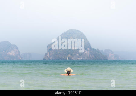 Femme au chapeau de paille dans la mer dans swiming Krabi Railey Beach donnant sur le port et les montagnes, la Thaïlande. Banque D'Images