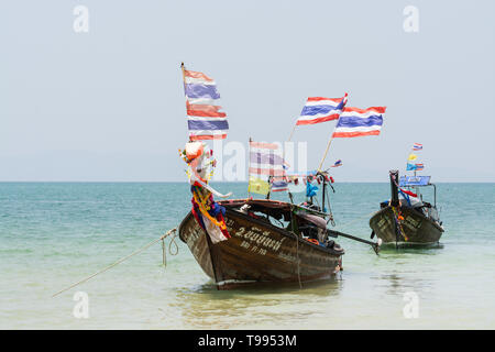 Krabi, Thaïlande - Mars 2019 : longue queue des bateaux en bois avec des drapeaux thaïlandais amarré à Railay beach. Banque D'Images