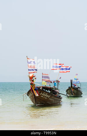 Krabi, Thaïlande - Mars 2019 : longue queue des bateaux en bois avec des drapeaux thaïlandais amarré à Railay beach. Orientation verticale. Banque D'Images