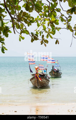 Krabi, Thaïlande - Mars 2019 : longue queue des bateaux en bois avec des drapeaux thaïlandais amarré à Railay beach. Orientation verticale. Banque D'Images