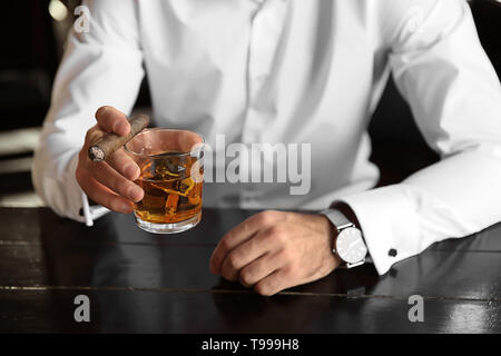 Jeune homme avec le verre de whisky et cigare dans un pub, closeup Banque D'Images