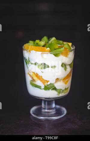 Dessert en couches dans un verre transparent, yaourt, orange, kiwi, noix sur un fond sombre. Le concept de la saine, bonne et simple des aliments sains Banque D'Images