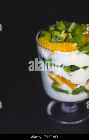 Dessert en couches dans un verre transparent, yaourt, orange, kiwi, noix sur un fond sombre. Le concept de la saine, bonne et simple des aliments sains Banque D'Images
