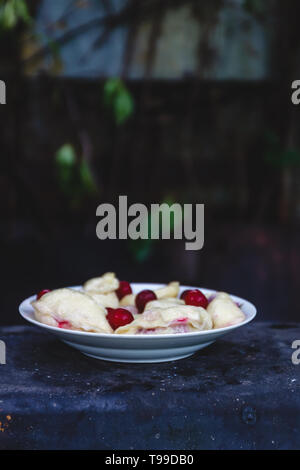 Quenelles avec les cerises dans un plat sur une sombre rétro arrière Banque D'Images