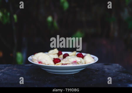 Quenelles avec les cerises dans un plat sur une sombre rétro arrière Banque D'Images