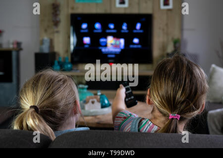 Vue arrière de deux enfants glissant à travers les applications sur une télévision intelligente. retour des enfants avec l'accent mis sur la télécommande. Le futurisme au quotidien Banque D'Images