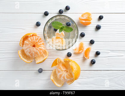 Verre d eau avec les tangerines et les bleuets sur table en bois blanc Banque D'Images