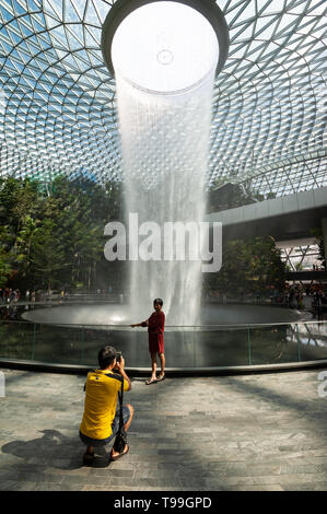 18.04.2019, Singapour, Singapour , - un homme photographies sa femme en face de la cascade dans le nouveau bijou à l'Aéroport International de Changi Terminal. T Banque D'Images