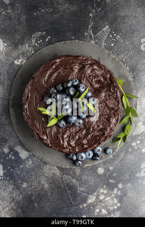 Haut de la table gâteau au chocolat avec les bleuets et les feuilles vertes sur fond gris foncé. Espace libre pour le texte, l'idée de gâteau d'anniversaire Banque D'Images