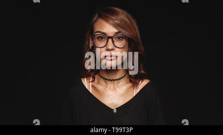 Femme à lunettes isolé sur fond noir. Portrait d'une femme à la mode avec des lèvres percé looking at camera. Banque D'Images