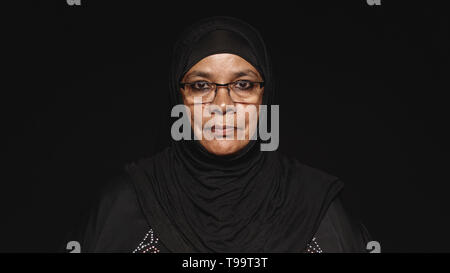 Portrait d'une femme musulmane en hijab isolé sur fond noir. Femme arabe portant des lunettes et d'un hijab noir looking at camera. Banque D'Images