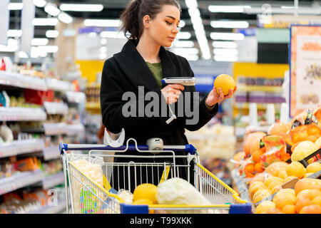 Young attractive woman holding de code à barres et systèmes de numérisation en magasin. Concept de gadgets et d'appareils modernes, département de fruits et légumes Banque D'Images