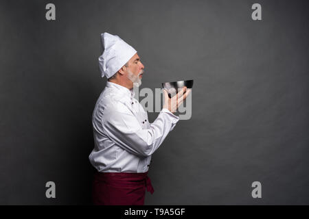 Smiling mature male chef avec bol dans les mains sur fond noir. Banque D'Images