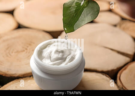 L'eau qui goutte de feuille en pot de crème sur fond de bois Banque D'Images