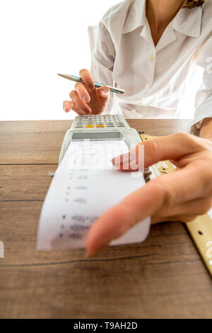 Femme sa comptabilité sur une machine avec un ajout manuel low angle view passé la bande de papier imprimé à ses doigts sur les touches numériques. Banque D'Images