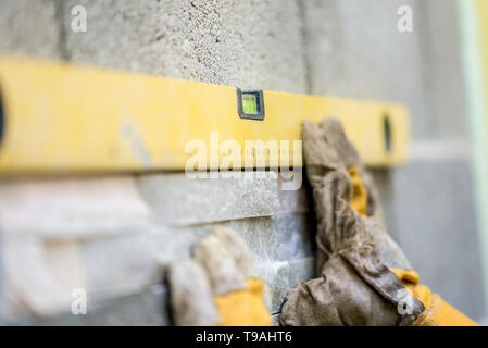 Gros plan du travailleur manuel en portant des gants protecteurs tenant une étiquette jaune contre un mur tout en plaçant la tuile et ornementales. De construction conceptuelle Banque D'Images