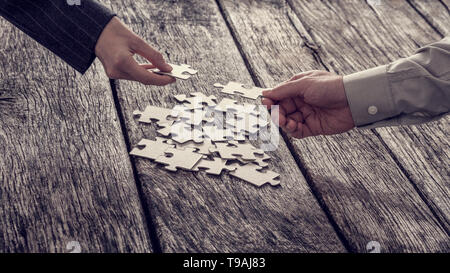 Deux mains différentes de gens d'affaires non identifiables pour atteindre des pièces de puzzle à partir de la pile. Banque D'Images