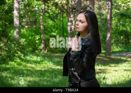 Belle fille portrait dans la forêt un jour de printemps. Femme avec black hairstyle et porte une veste en cuir. Le bois dans l'arrière-plan. Close up Banque D'Images