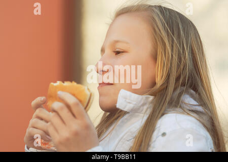 Happy teen girl eating a burger on city street Banque D'Images