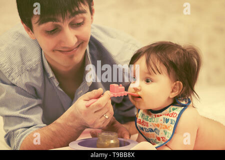 Heureux père nourrir bébé girl at home Banque D'Images