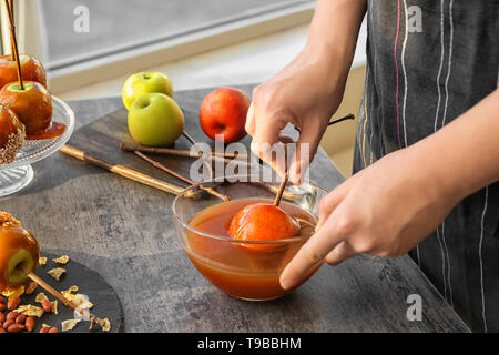 Femme trempant dans apple bol en verre avec le caramel à table gris Banque D'Images