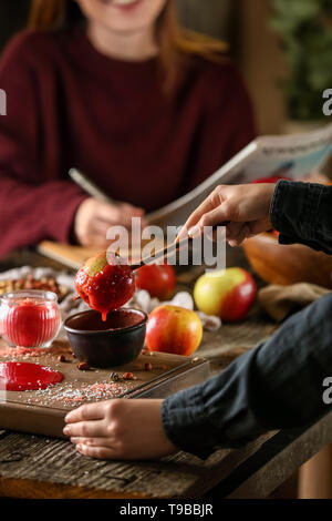 Femme trempant dans un bol d'apple avec le caramel sur table en bois Banque D'Images