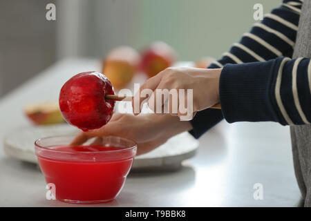 Femme trempant dans un bol d'apple avec le caramel sur table lumineuse Banque D'Images